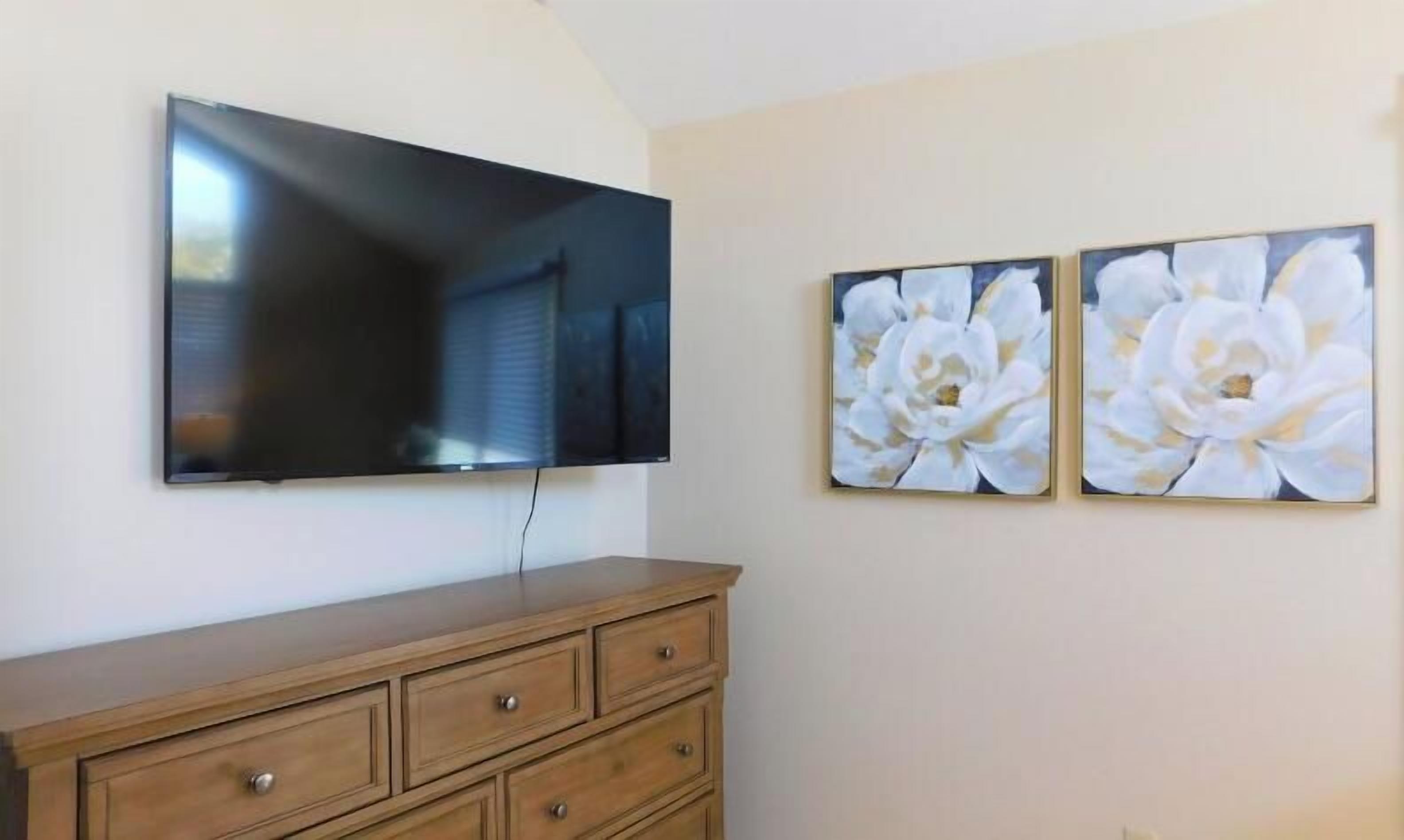 A flat-screen TV mounted on a wall above a wooden dresser with drawers.