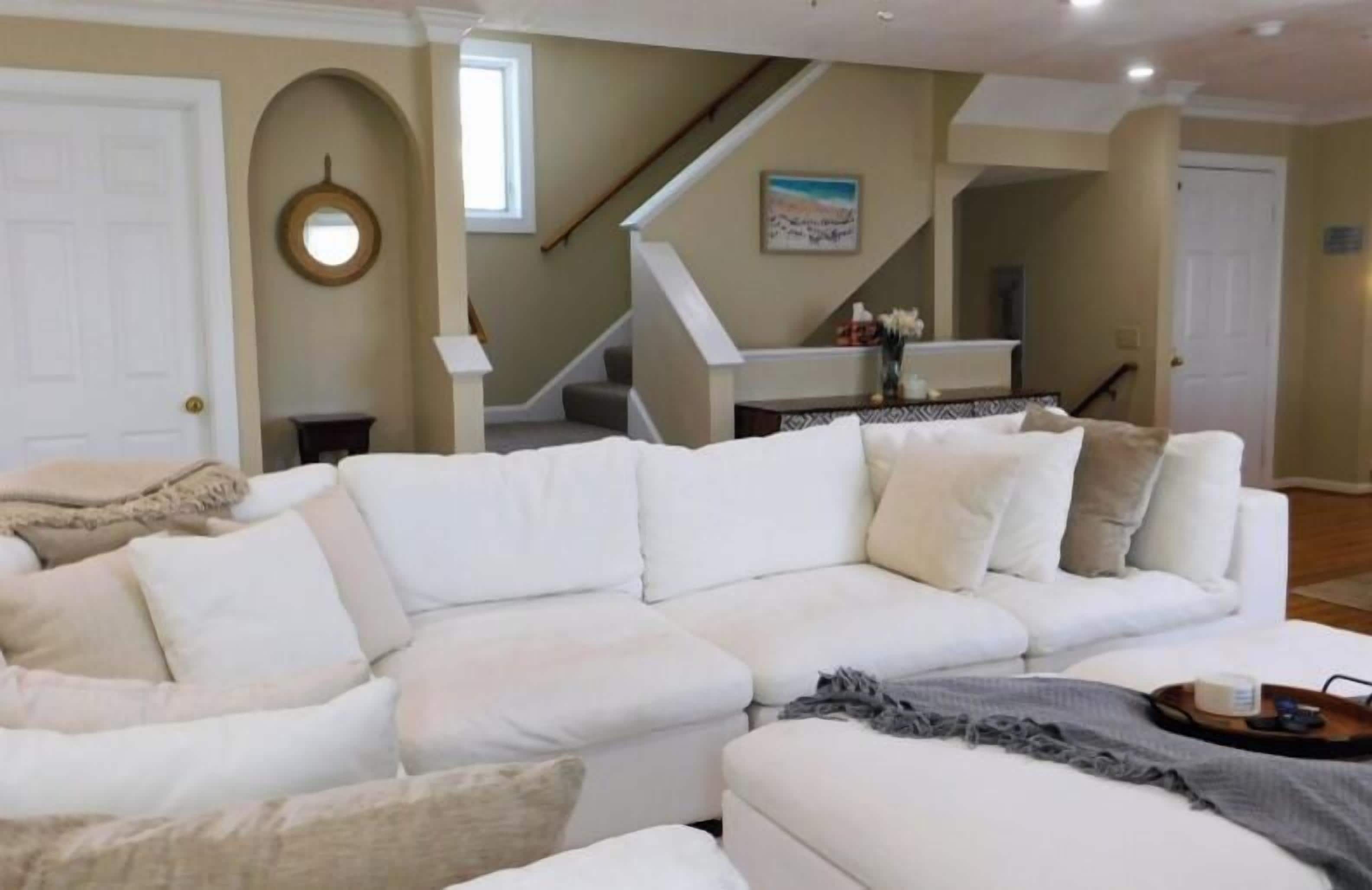 A living room with a white sectional sofa, a coffee table, and a staircase in the background.