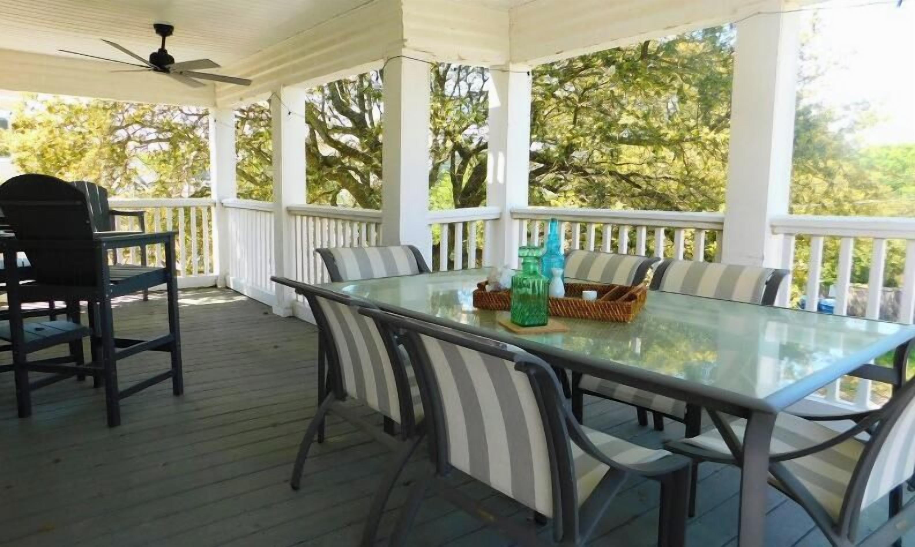 A covered outdoor dining area with a glass table and striped chairs, surrounded by a white railing.