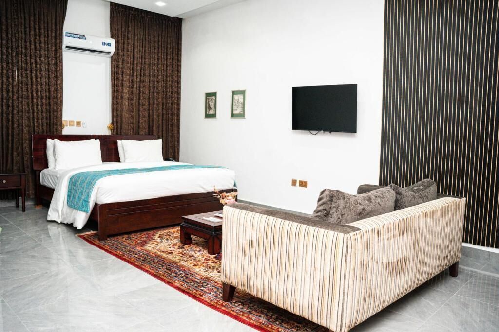 A modern bedroom with a bed, a sofa, a TV, and an air conditioning unit.