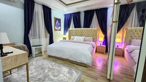 A hotel room with a large bed, two bedside tables with lamps, a small round table, and a chair. - The Enclave Apartment (Asaba)