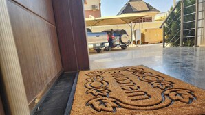 A doormat with a decorative design, a vehicle parked outside, and a building with a sloped roof in the background. - The Enclave Apartment (Asaba)
