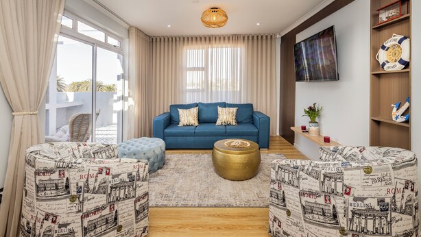 Un salon avec un canapé bleu, des poufs à motifs, une table basse ronde et une grande fenêtre avec des rideaux.