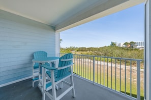 A balcony with a table and chairs, a view of the beach, and a building in the background. - Grand Caribbean 117 (Orange Beach)