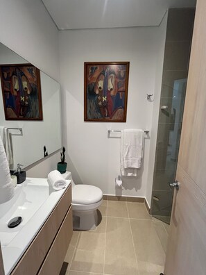A bathroom with a sink, toilet, and shower. There are two paintings on the wall. - Eira Studios Santa Marta by Xarm Apartments (Santa Marta)