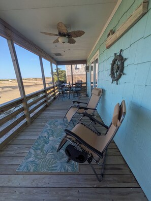 A covered outdoor seating area with a ceiling fan, a table with chairs, a decorative wall piece, and a view of the beach. - Cozy Oceanside Cottage in Frisco (Frisco)