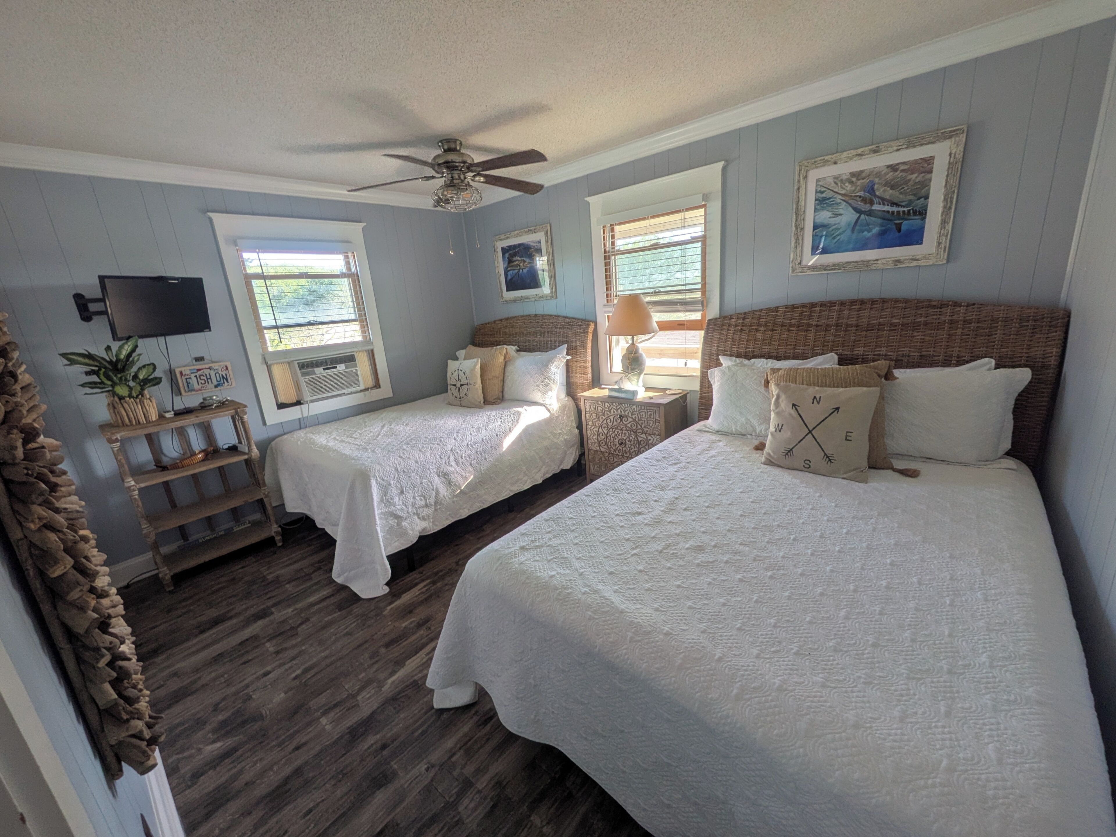 A bedroom with two beds, a ceiling fan, a TV, and a window with blinds.