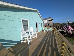 A turquoise house with a wooden deck, white chairs, and an American flag.