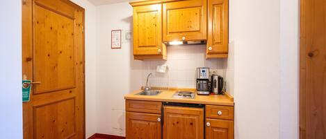 A compact kitchen with wooden cabinets, a sink, a coffee maker, and a stove.