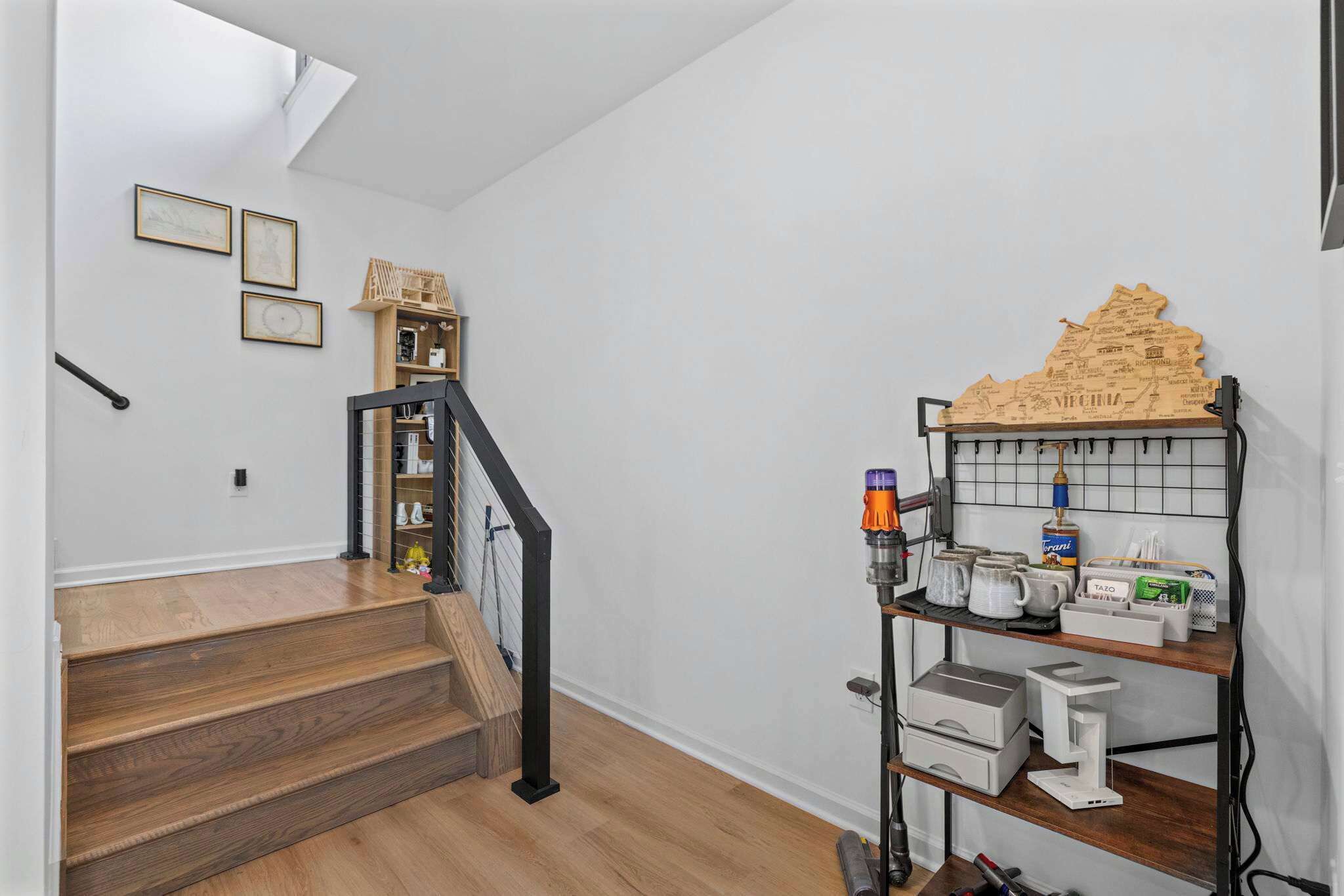 A staircase with wooden steps and a black railing, leading to a room with a white wall and a shelf with various items.