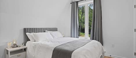 Un dormitorio con cama, mesita de noche, lámpara y ventana con cortinas.