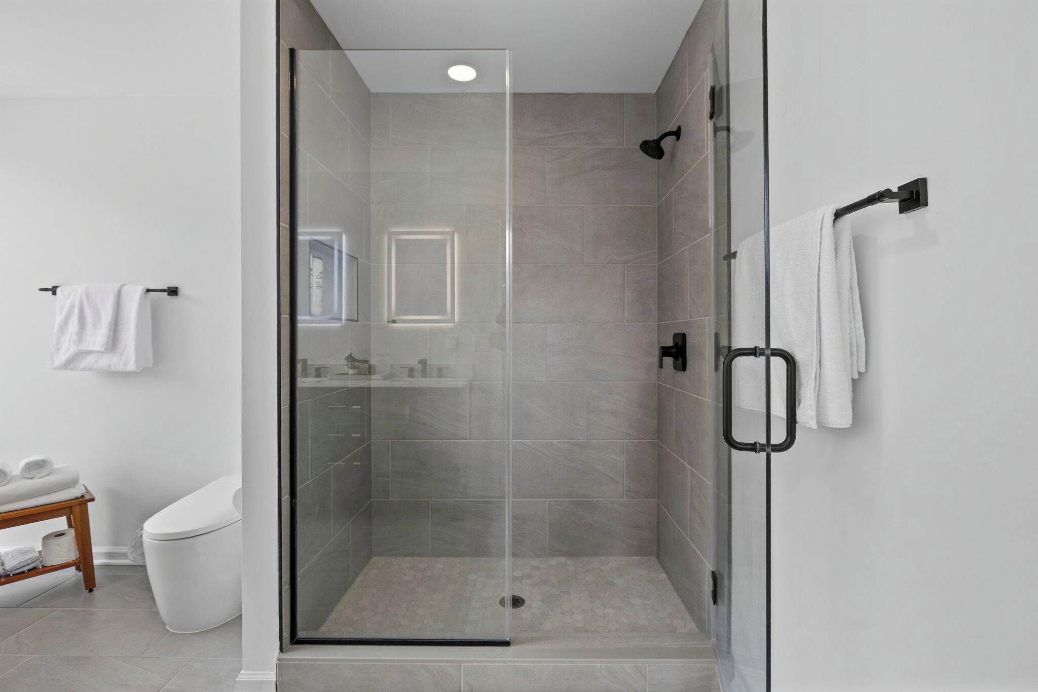 Et moderne badeværelse med en glasafskærmet brusekabine, toilet og et lille underskab med spejl.