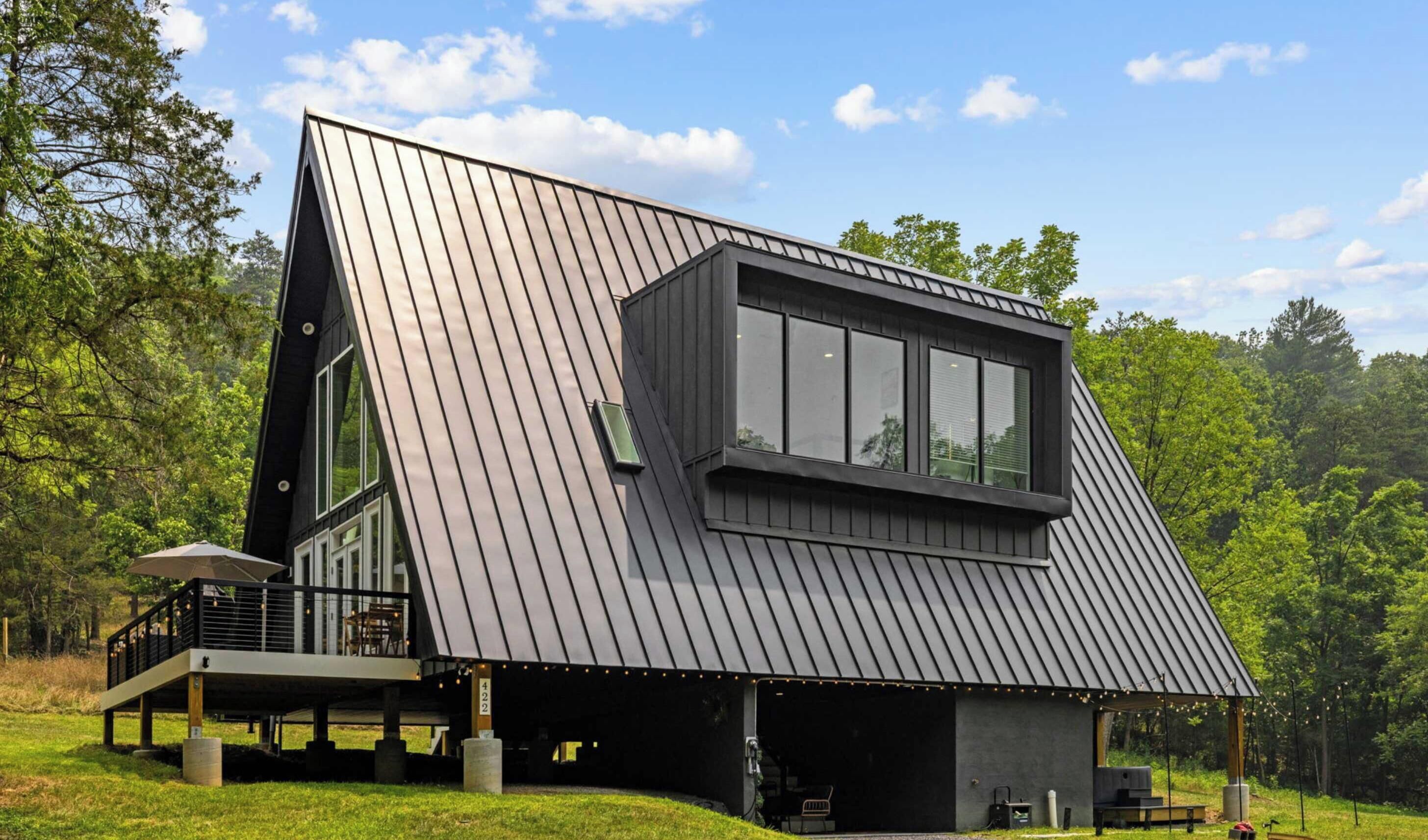 A modern house with a sloped metal roof, large windows, and a deck area.