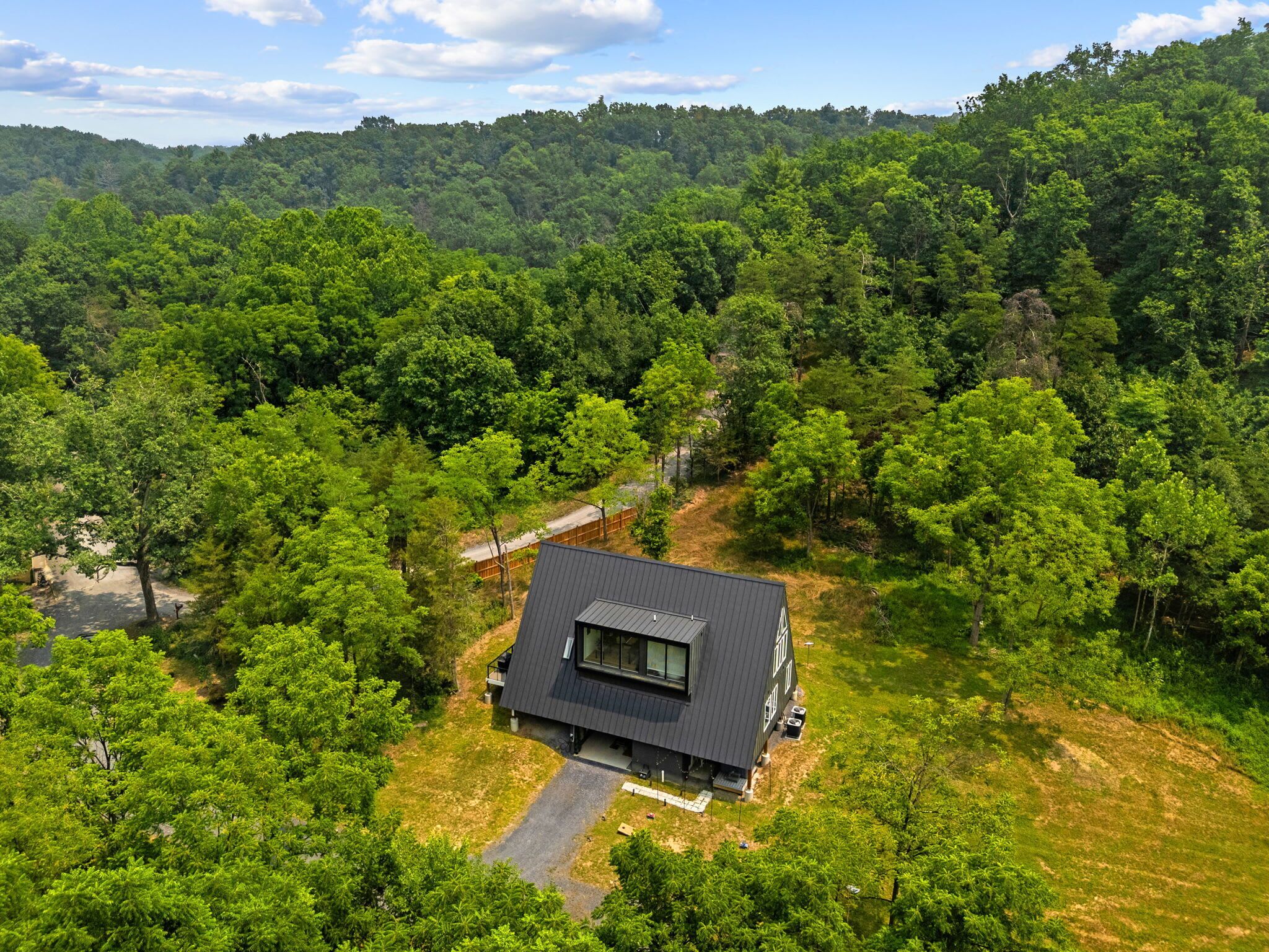 A modern house with a dark roof, surrounded by dense forest and a clear sky.