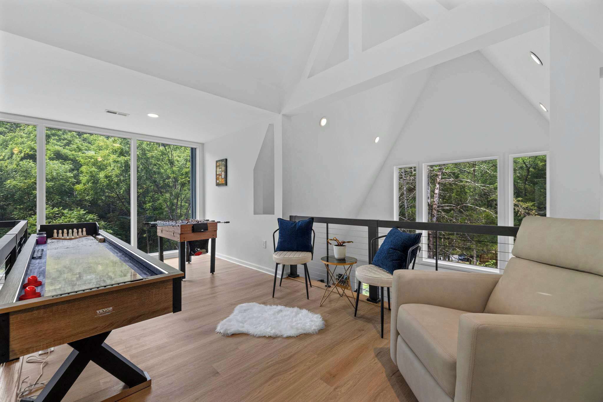 A modern living room with a foosball table, a sofa, and a balcony with a view of trees.