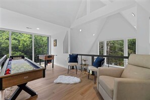 A modern living room with a foosball table, a sofa, and a balcony with a view of trees. - Chalet w/Hot Tub, Deck, Game Room & EV Charger (Stephens City)