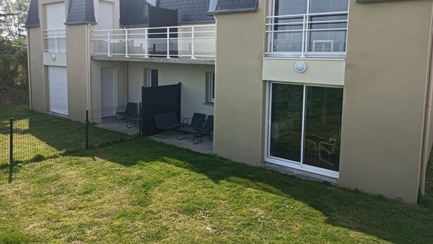 Un edificio de dos plantas con balcón, ventanas amplias y una zona de estar exterior con cerramiento.