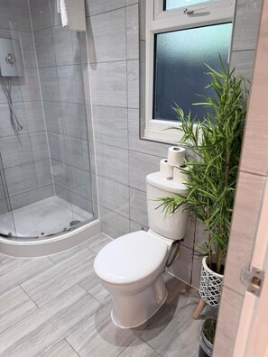 Ein Badezimmer mit Dusche, Toilette und einem Fenster.