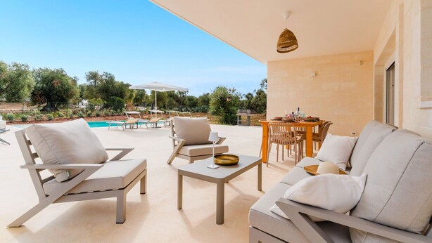 An outdoor seating area with lounge chairs, a table, and a view of a swimming pool. - Villa delle Stelle by Perle di Puglia (Carovigno)