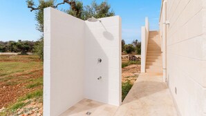 A white-walled outdoor shower area with a tiled floor, a metal shower head, and a door leading to a staircase. - Villa delle Stelle by Perle di Puglia (Carovigno)