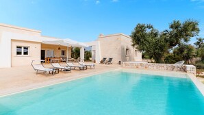 A pool area with lounge chairs and umbrellas, a stone wall, and a building with a patio. - Villa delle Stelle by Perle di Puglia (Carovigno)