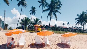 A beach with palm trees, beach chairs, and umbrellas. - Makia Beach Resort Luxo - Muro Alto-10 Piscinas (Ipojuca)
