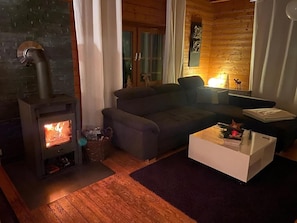 Uma sala de estar acolhedora com lareira a lenha, sofá, mesa de centro e manto da lareira.