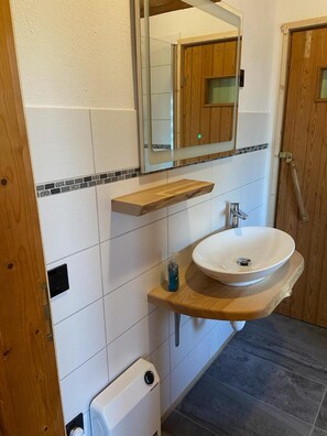 Une salle de bain avec un lavabo blanc, un meuble-lavabo en bois, un miroir et un espace douche.