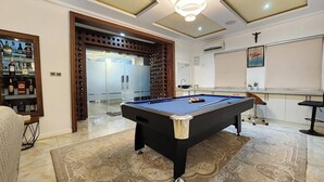 Een biljart tafel in een goed verlichte kamer met een kamerkleed met patroon, een bar met flessen en een grote spiegel.