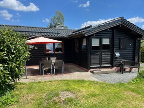 En timmerstuga med en uteplats, utomhusmöbler och ett rött parasoll.