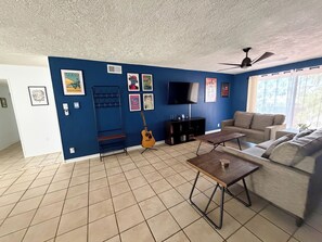 Una sala de estar con una pared azul, una guitarra, un televisor, un sofá y un ventilador de techo.