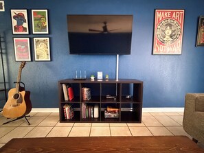 Una sala de estar con televisor, estantería, guitarra y obras de arte en la pared.