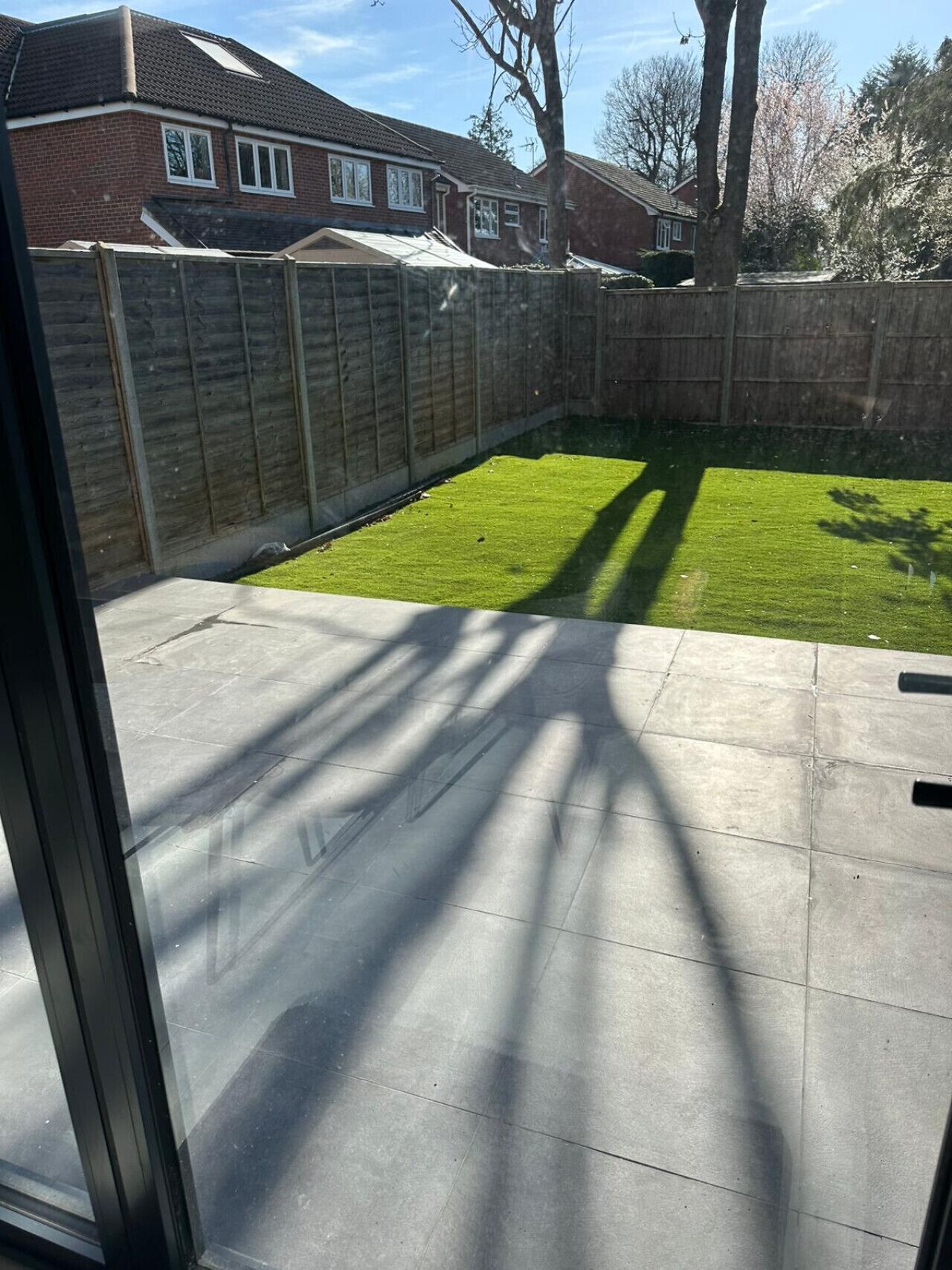 A backyard with a grassy area, a wooden fence, and a house in the background.