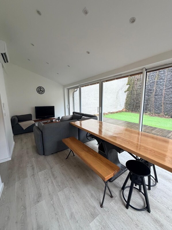 Una sala moderna con una amplia mesa de madera, sofás grises y un televisor.