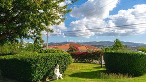 Un jardín bien cuidado con una estatua, setos podados con esmero y vistas a edificios y montañas distantes.