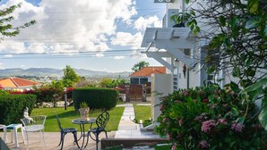 Un patio con mobiliario exterior, un pabellón blanco y vistas a un pueblo y montañas.
