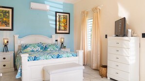 Un dormitorio con cama, mesitas de noche, cómoda, ventilador de techo y dos cuadros en la pared.