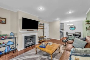 Ein Wohnzimmer mit Kamin, Fernseher, Couchtisch, Sofa und einem Essbereich mit Stühlen.