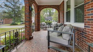 A covered porch with a brick wall, a seating area with cushions, and a view of the street. - 4BR Retreat w/ Game Shed | Near Downtown (West Columbia)