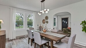 A dining area with a wooden table, grey upholstered chairs, a vase with flowers, and a modern light fixture. - 4BR Retreat w/ Game Shed | Near Downtown (West Columbia)
