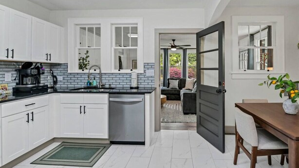 A modern kitchen with white cabinets, a dishwasher, and a coffee maker. There is a dining area with a table and chairs, and a door leading to a living space. - 4BR Retreat w/ Game Shed | Near Downtown (West Columbia)