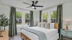 A bedroom with a bed, a nightstand, a lamp, a ceiling fan, and a window with curtains. - 4BR Retreat w/ Game Shed | Near Downtown (West Columbia)
