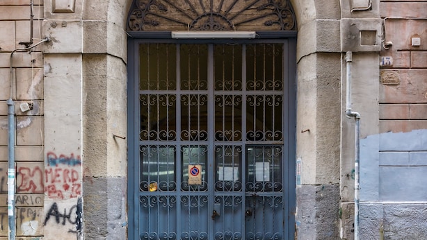 A stone building with a large arched entrance, a metal door with bars, and a cobblestone street. - Wide and Arty at Spanish Quarter (Naples)