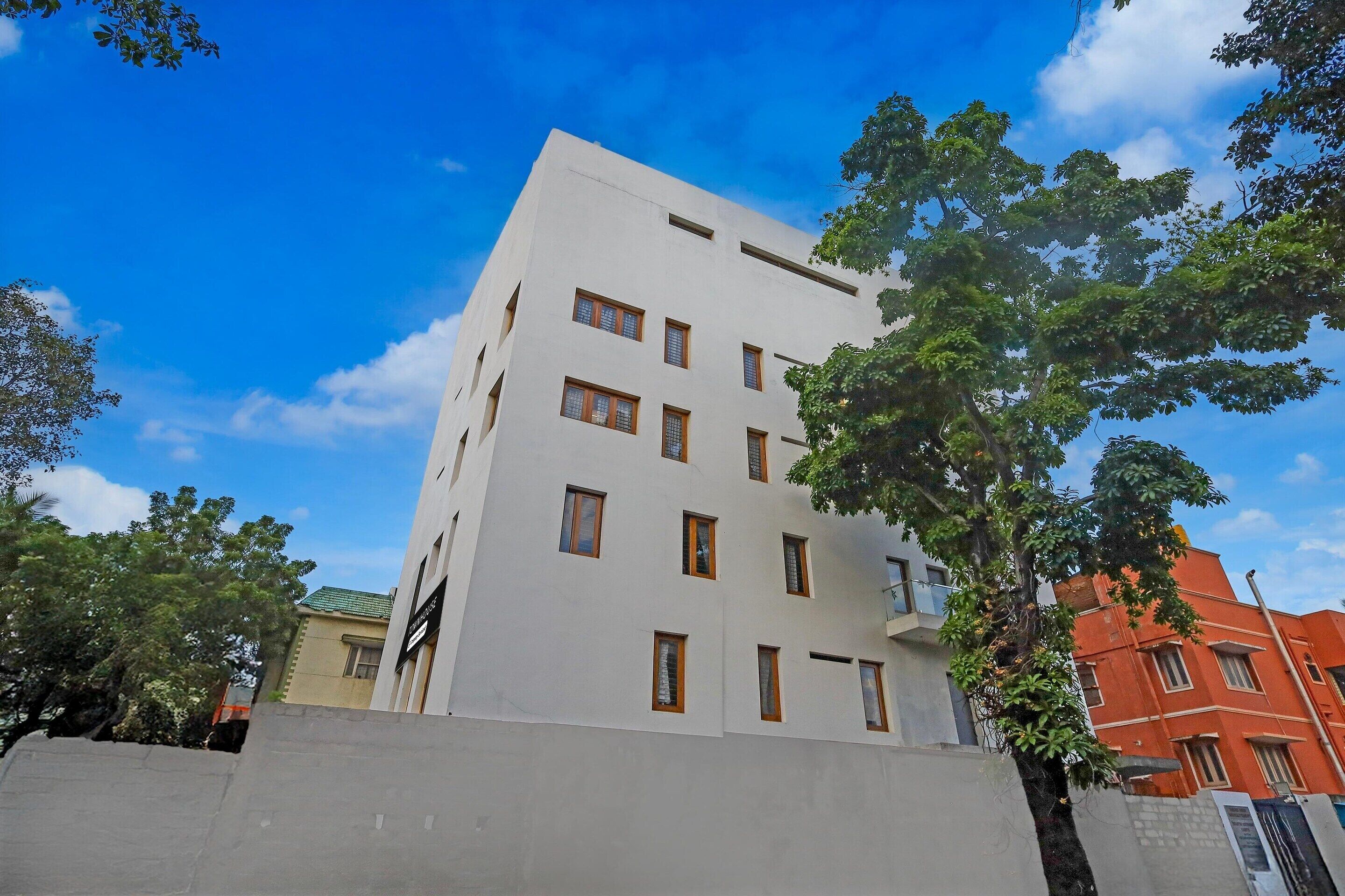 A multi-story building with a flat facade, rectangular windows, and a visible tree in the foreground.