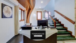 A reception desk labeled 'TOWNHOUSE' with a company-serviced sign, a desktop computer, a printer, and a monitor. A staircase with green carpeted steps and wooden railings is visible in the background. - Deluxe k.k Nagar Residency (Chennai)