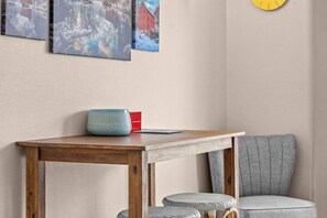 Eine Ecke eines Raumes mit einem Holztisch, einem blauen und roten Gegenstand darauf, einem grauen Stuhl und einer Wand mit drei gerahmten Bildern.