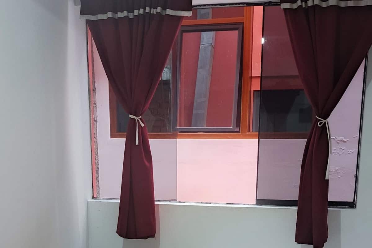A bedroom with a bed, a nightstand, a window with curtains, and patterned flooring.
