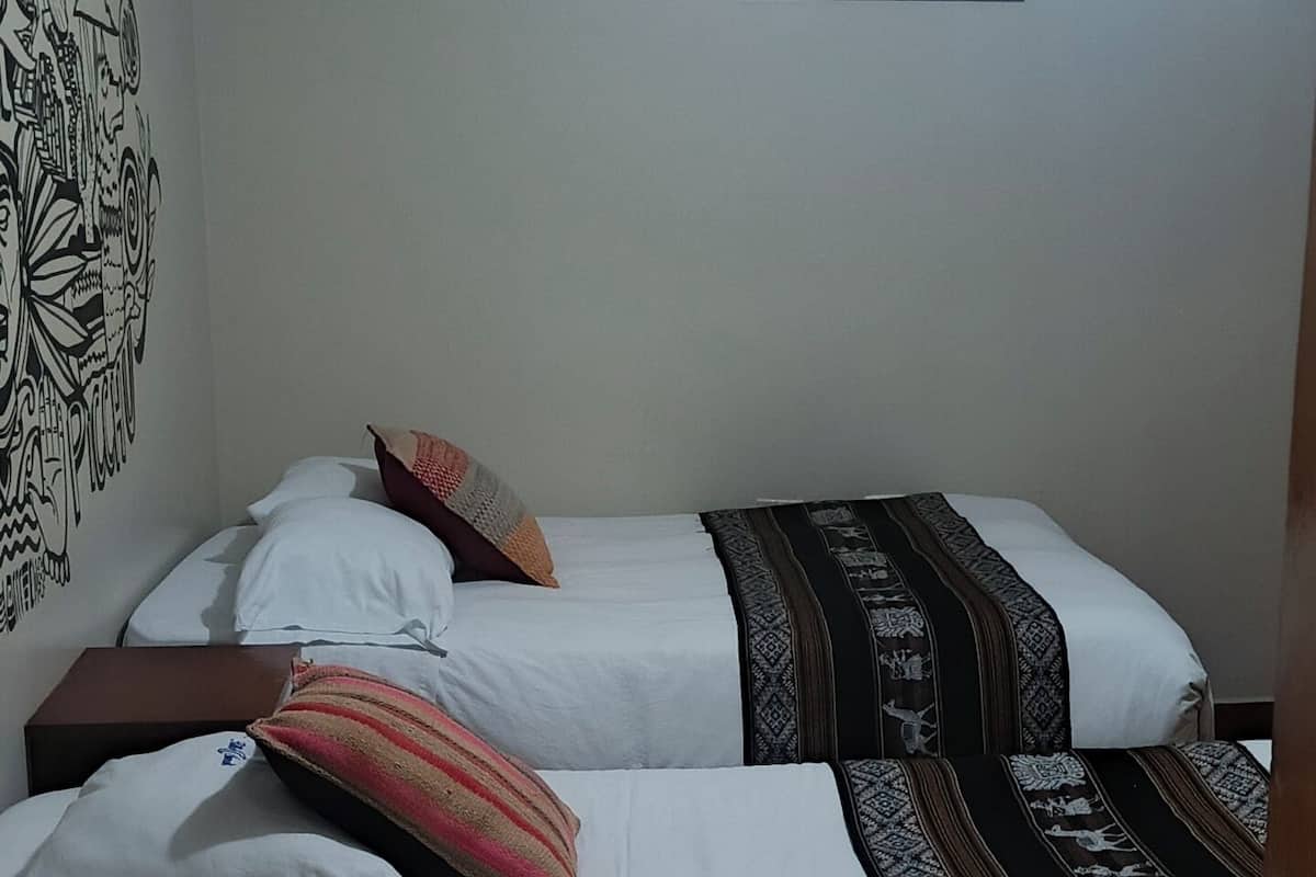 A room with two beds, a wooden floor, a wall with a black and white mural, and a ceiling light.
