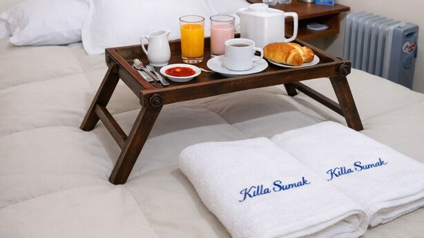 Camera d'albergo con un letto, un vassoio con prodotti per la colazione e asciugamani con il nome dell'hotel.