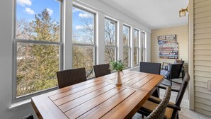 A sunroom with large windows, a wooden table, wicker chairs, and a poster on the wall. - Luxury Lake Vacation at Emerald Pointe (Hollister)